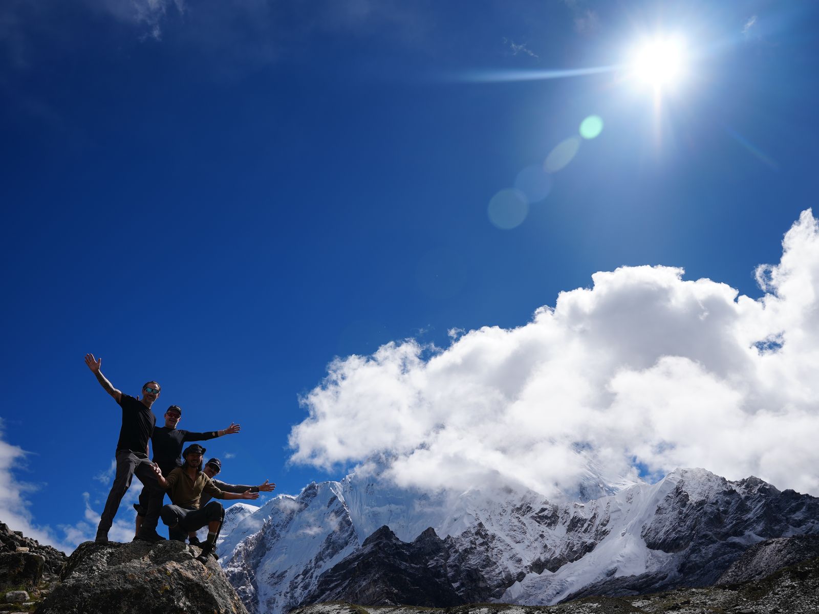 Lane Belone, Ashley Johnson, Andy Hooper and Lee Smith with arms outstretched on a rock below snow peaks on the way to Everest Base Camp